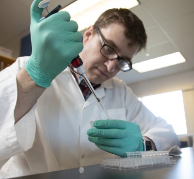 a person in a lab coat and gloves holding a pipette