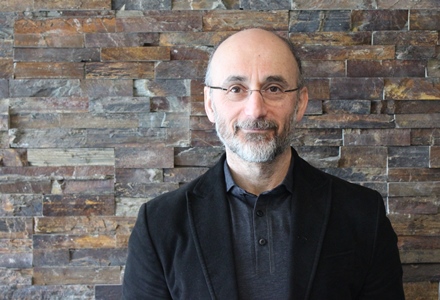 a person in a black jacket and glasses standing in front of a brick wall