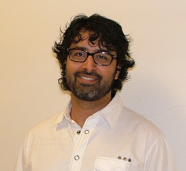 a person with a beard and glasses standing in front of a white wall