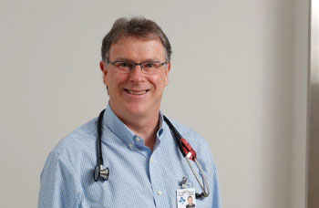 une personne dans une chemise bleue et des lunettes se tient devant un mur blanc