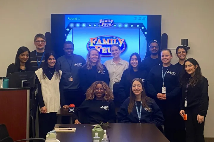 Members of the Blueprint team standing and sitting in front of a television screen showing the Family Feud game