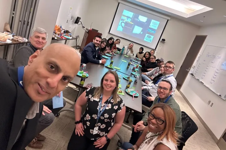Members of the blueprint team sated around a table with a screen in the background showing the Family Feud game