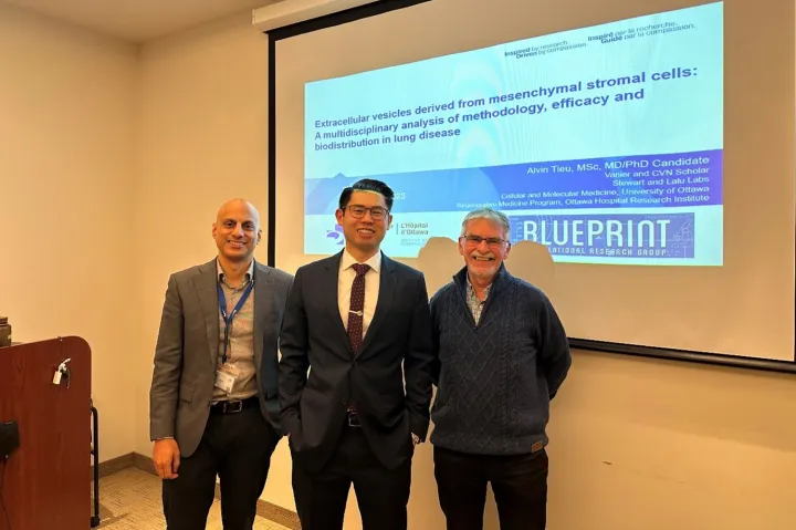 Three people standing in front of a screen with the title Extracellular vesicles derived from mesenchymal stromal cells: A multidisciplinary analysis of methodology, efficacy and biodistribution in lung disease