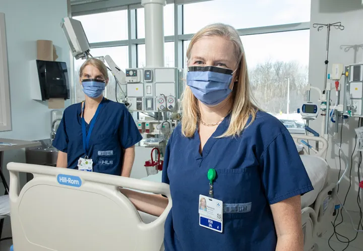 Two members of the critical care research team stand beside a patient’s bed
