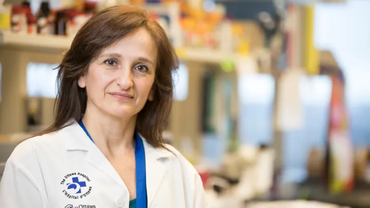 A woman with shoulder-length brown hair stands in a lab and smiles