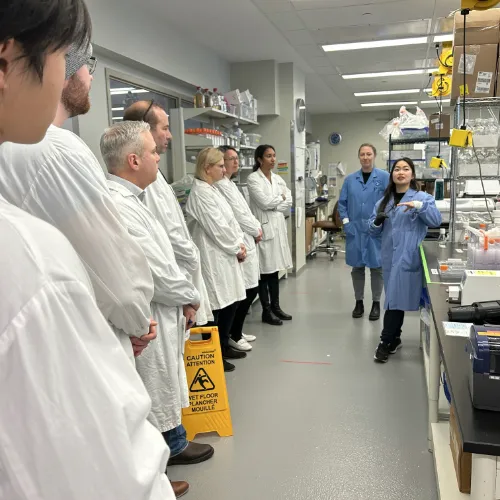 A group of people standing in a lab listen to researchers