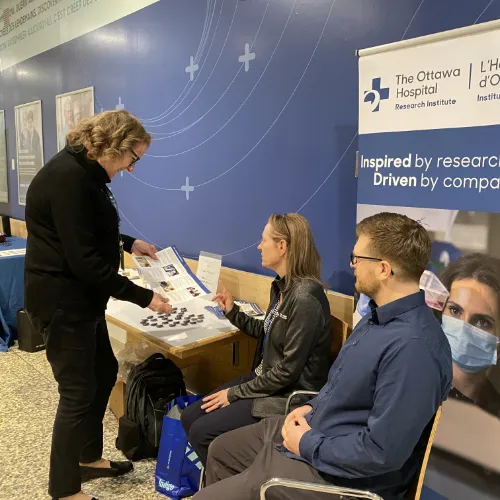 Two people sit at a kiosk while a third browses the material