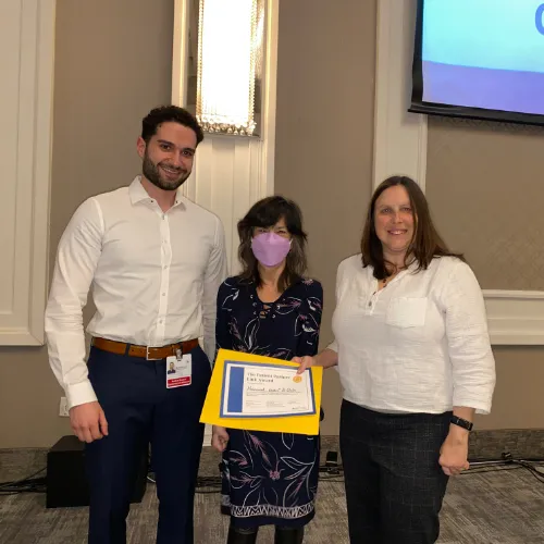 A man and two women stand together holding an award