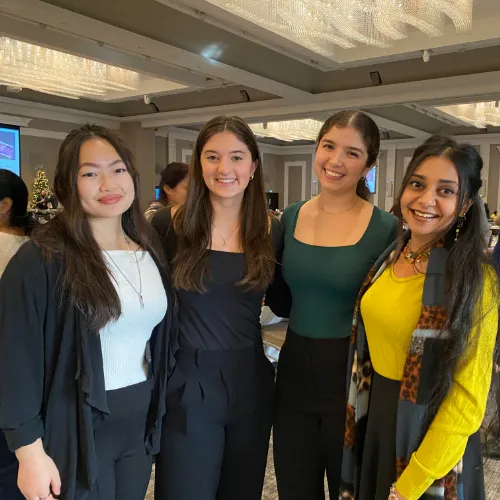 Four women stand together and smile