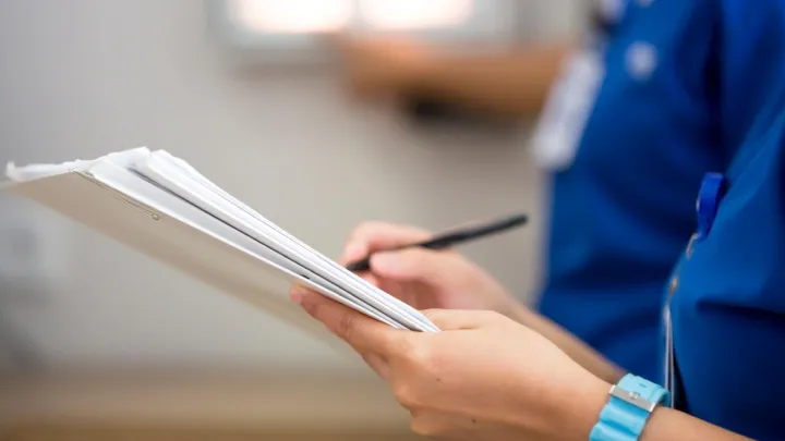 A close up of a nurse's hands writing on a clipboard
