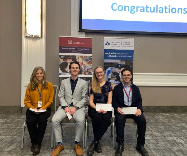 Four people holding awards sit on chairs