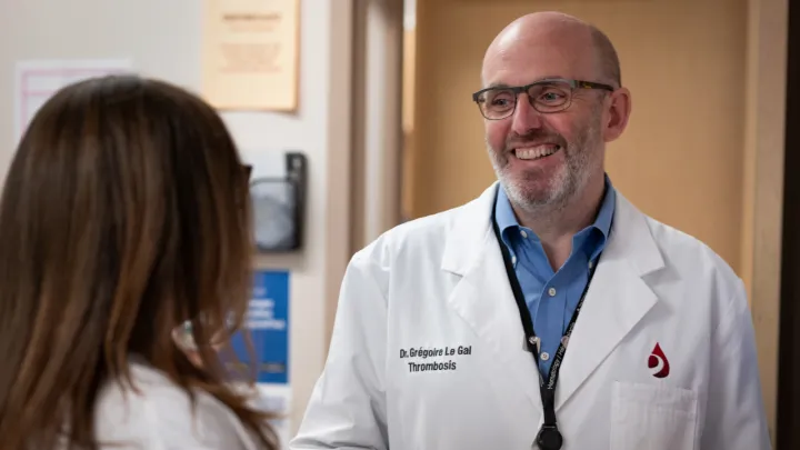 A man wearing glasses and a lab coat smiles at woman who has her back to the camera