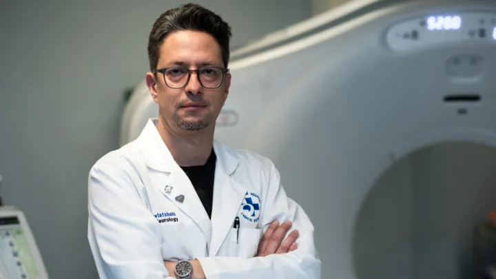 Man in lab coat stands in front of a CT scanner