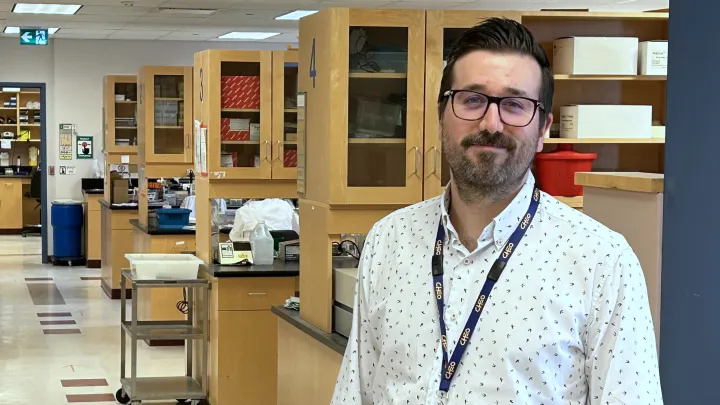 Man with glasses stands in front of a row of lab benches