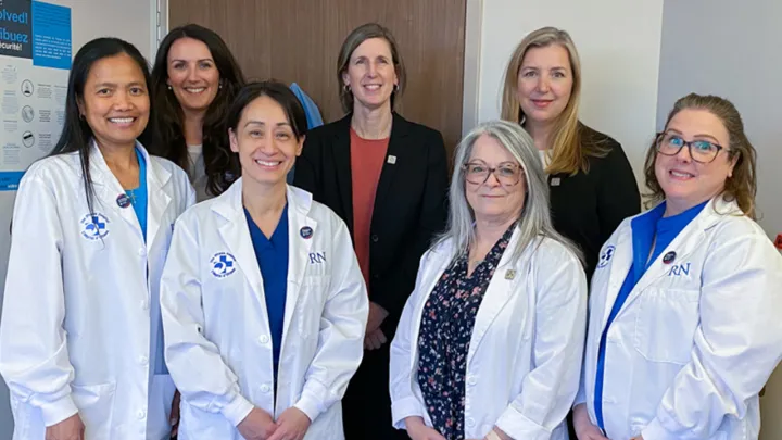 Seven people pose for a photo in a hospital room.