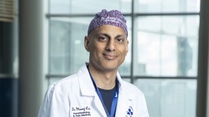 Man in surgical hat and lab coat looks at camera