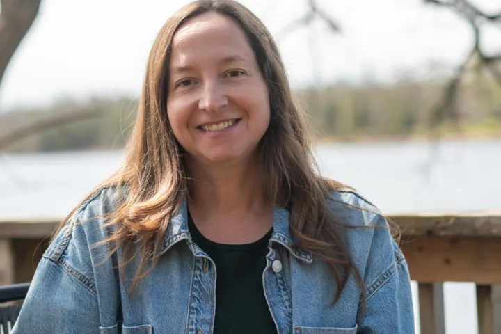 A smiling woman standing in front of a lake