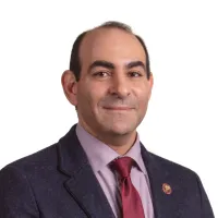 A headshot of a man wearing a red tie and light purple shirt 