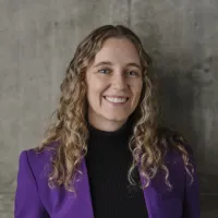 A woman wearing a purple blazer smiles at the camera