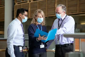 Three people look at a folder in a hospital hallway