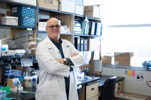 A smiling man with his arms crossed leans against a lab bench