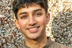 A young man with dark brown hair smiles at the camera