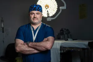 A male doctor stands in an operating room with his arms crossed
