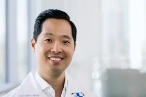 A man wearing a white lab coat smiles at the camera