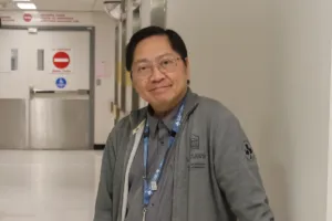 A man stands in a hallway at a hospital and leans against the wall