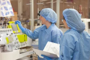 Two nurses wearing scrubs and surgical caps work together in a lab