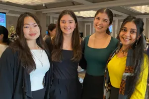 Four women stand together and smile