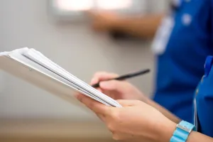 A close up of a nurse's hands writing on a clipboard