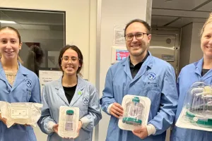 Four people wearing lab coats hold lab equipment
