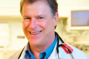 A man with a stethoscope around his neck smiles at the camera