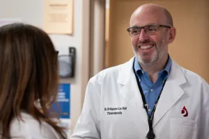 A man wearing glasses and a lab coat smiles at woman who has her back to the camera