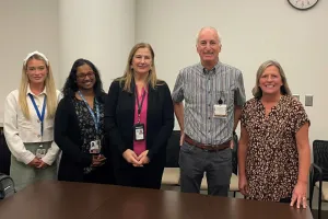 Five people stand together in an meeting room and smile