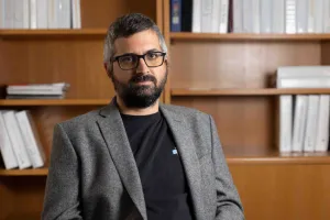 A man sits on a chair with a bookshelf behind him