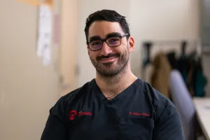 A man wearing scrubs smiles at the camera