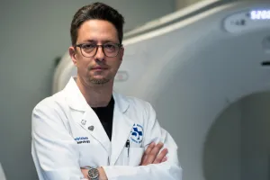 Man in lab coat stands in front of a CT scanner
