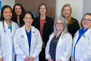 Seven people pose for a photo in a hospital room.