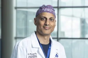 Man in surgical hat and lab coat looks at camera