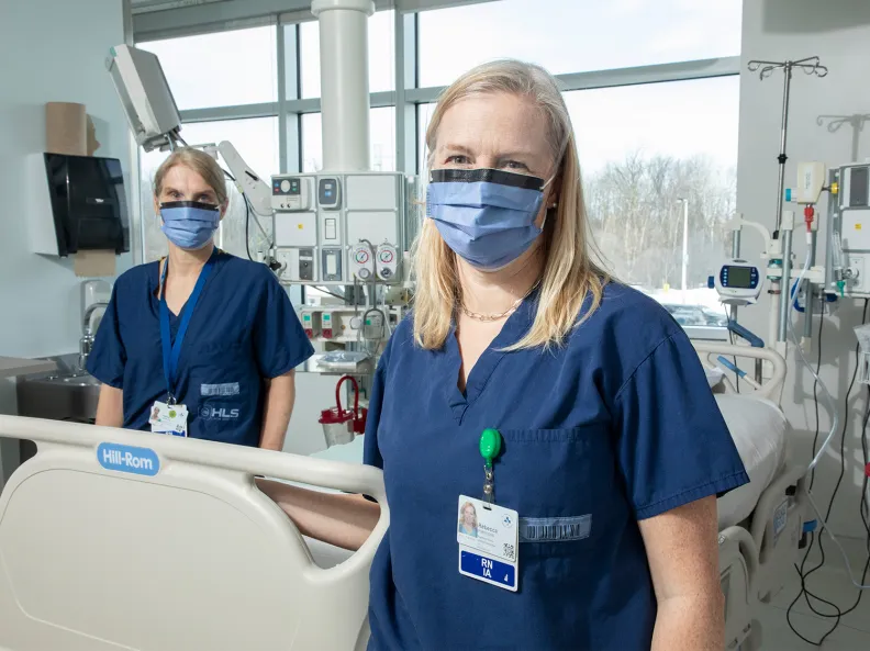 Two members of the critical care research team stand beside a patient’s bed