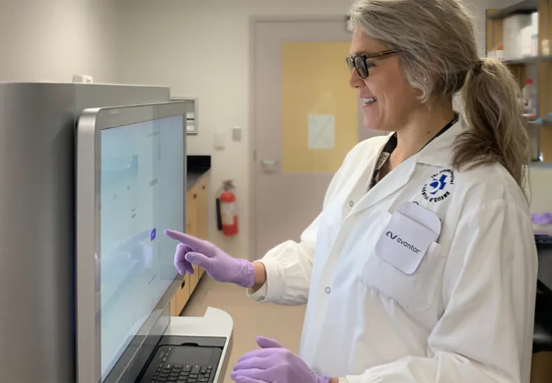 A person in a white lab coat looks at a screen.