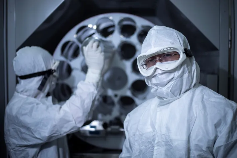 Two people wearing hooded suits and googles in a lab