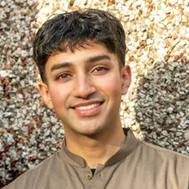 A young man with dark brown hair smiles at the camera