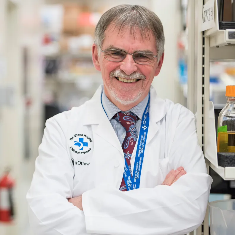 A man in a lab coat smiles as he leans against a wall