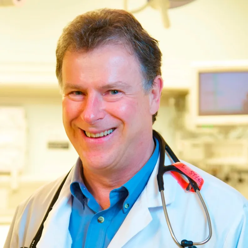 A man with a stethoscope around his neck smiles at the camera
