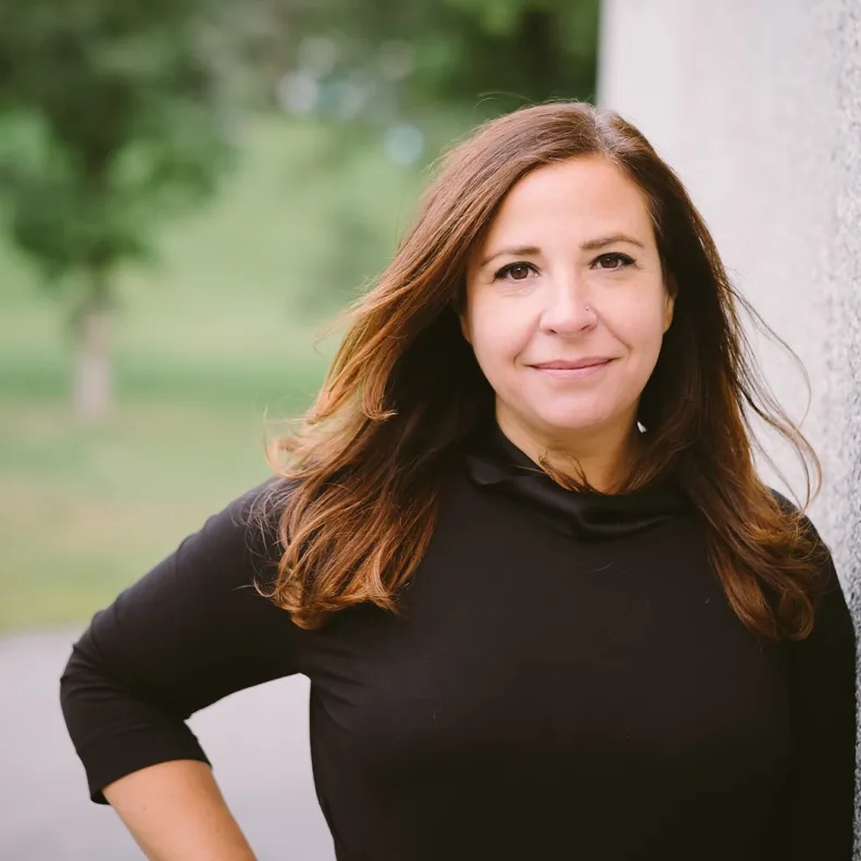 A woman stands outside and smiles at the camera