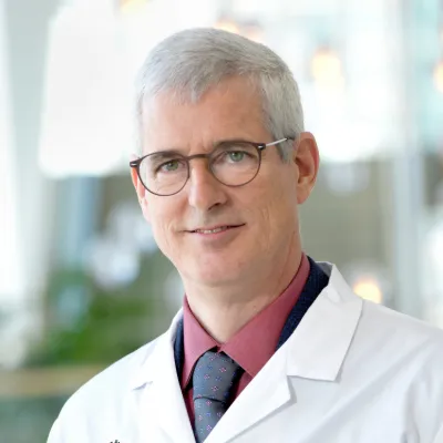 A man wearing a lab coat and glasses smile at the camera