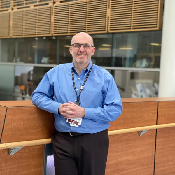 A man wearing glasses and a blue shirt smiles at the camera